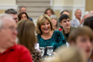Donna Ward is at a table surrounded by people. She smiles in surprise as her name is called as the state's 2026 Educational Support Professional of the Year.