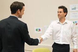 Two men shaking hands across desk