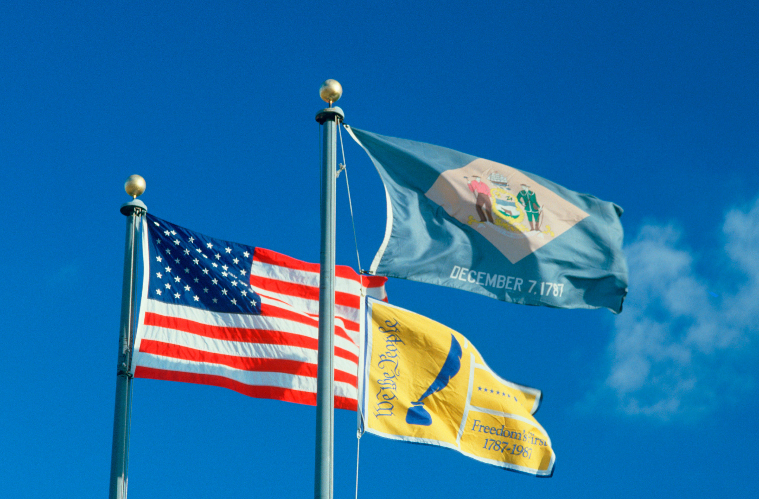 United States flag and State Flag of Delaware flying in the wind